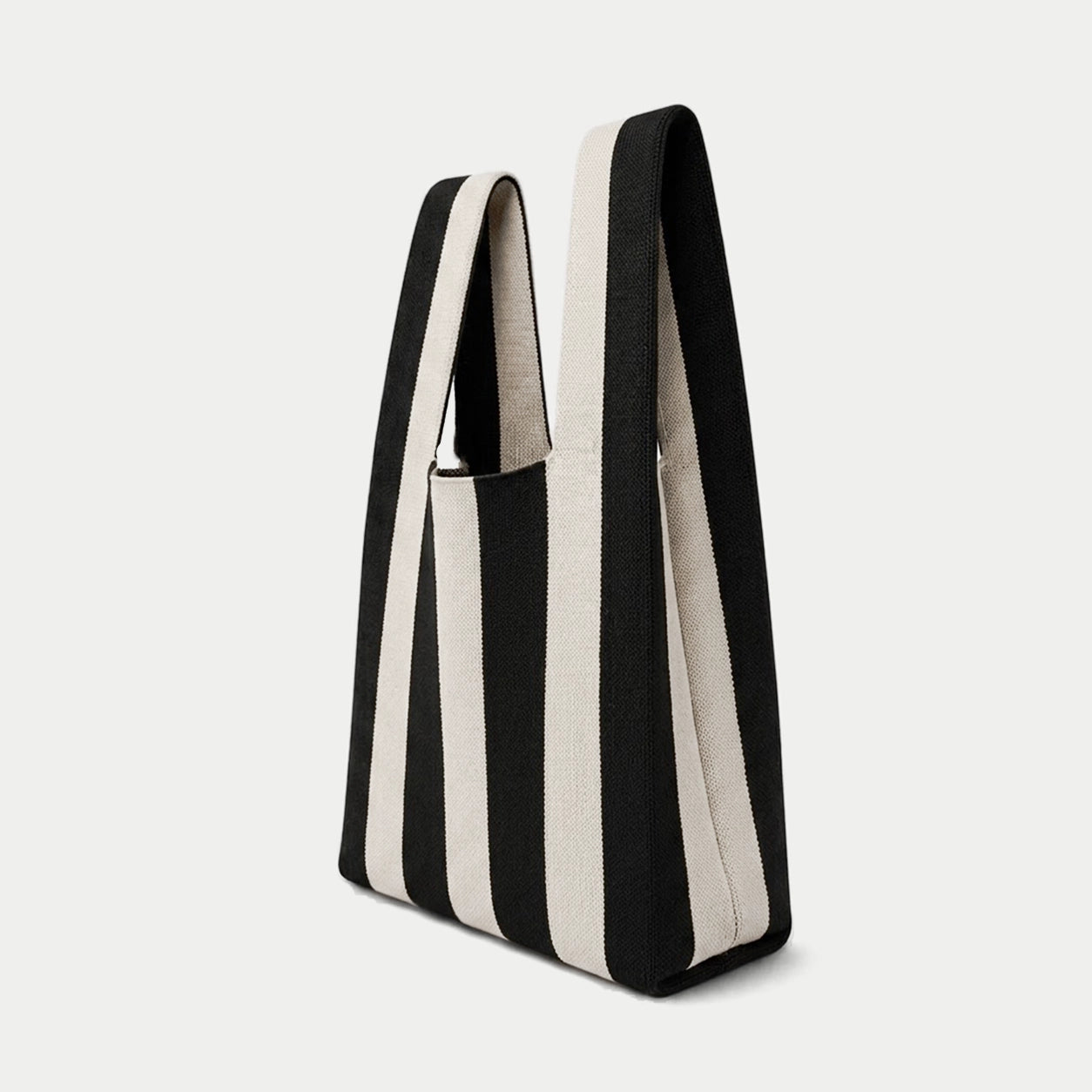 Side view of black and white vertical stripe knitted tote bag showing the structured silhouette, handle design and textured knit construction.