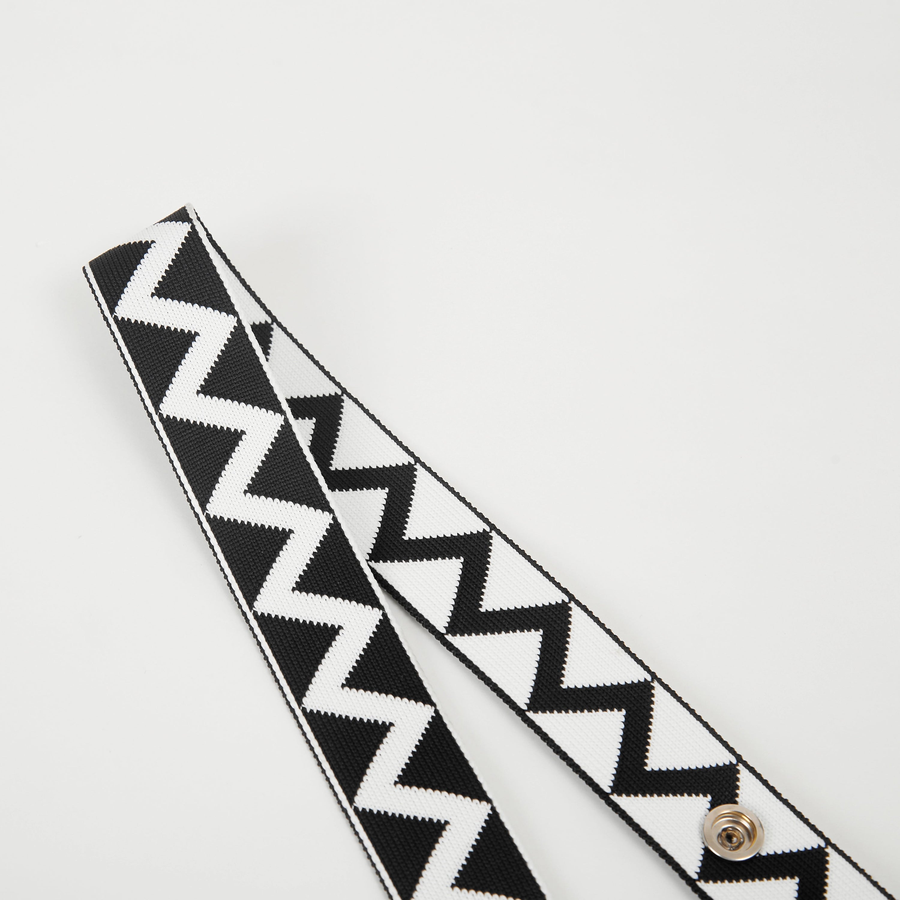 Close-up of black zigzag pattern bag strap showing geometric design, snap buttons, and textured knit surface.