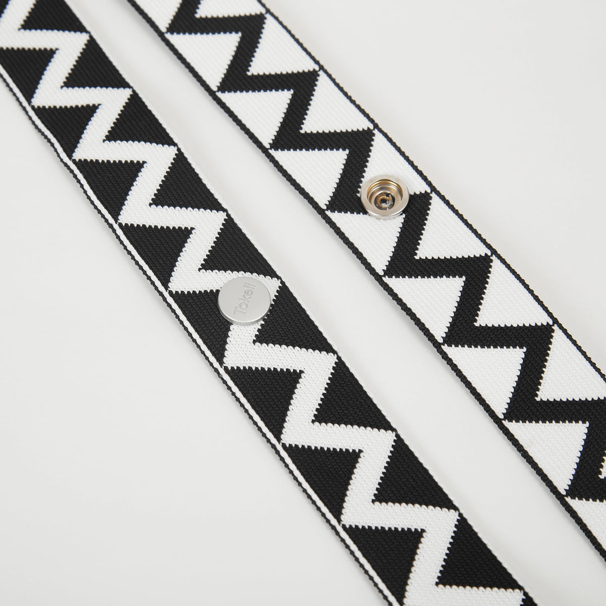 Detail view of black patterned bag strap highlighting the zigzag motif and metal fastening details.