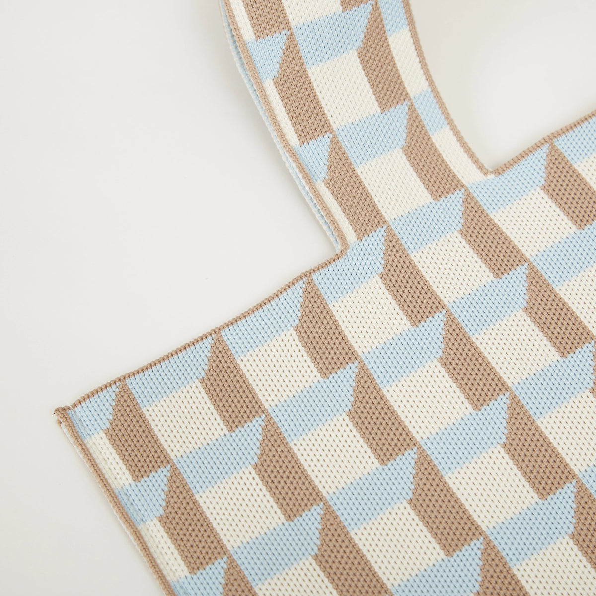Close-up of blue and camel geometric check pattern on knitted tote bag showing textured fabric detail.
