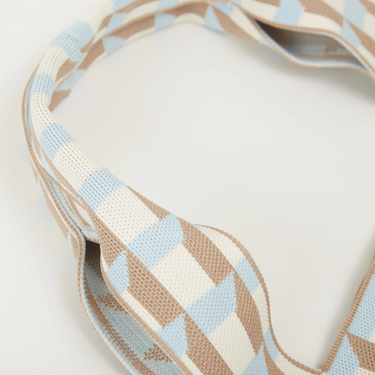 Close-up of curved knitted handles on blue and camel geometric check tote bag.