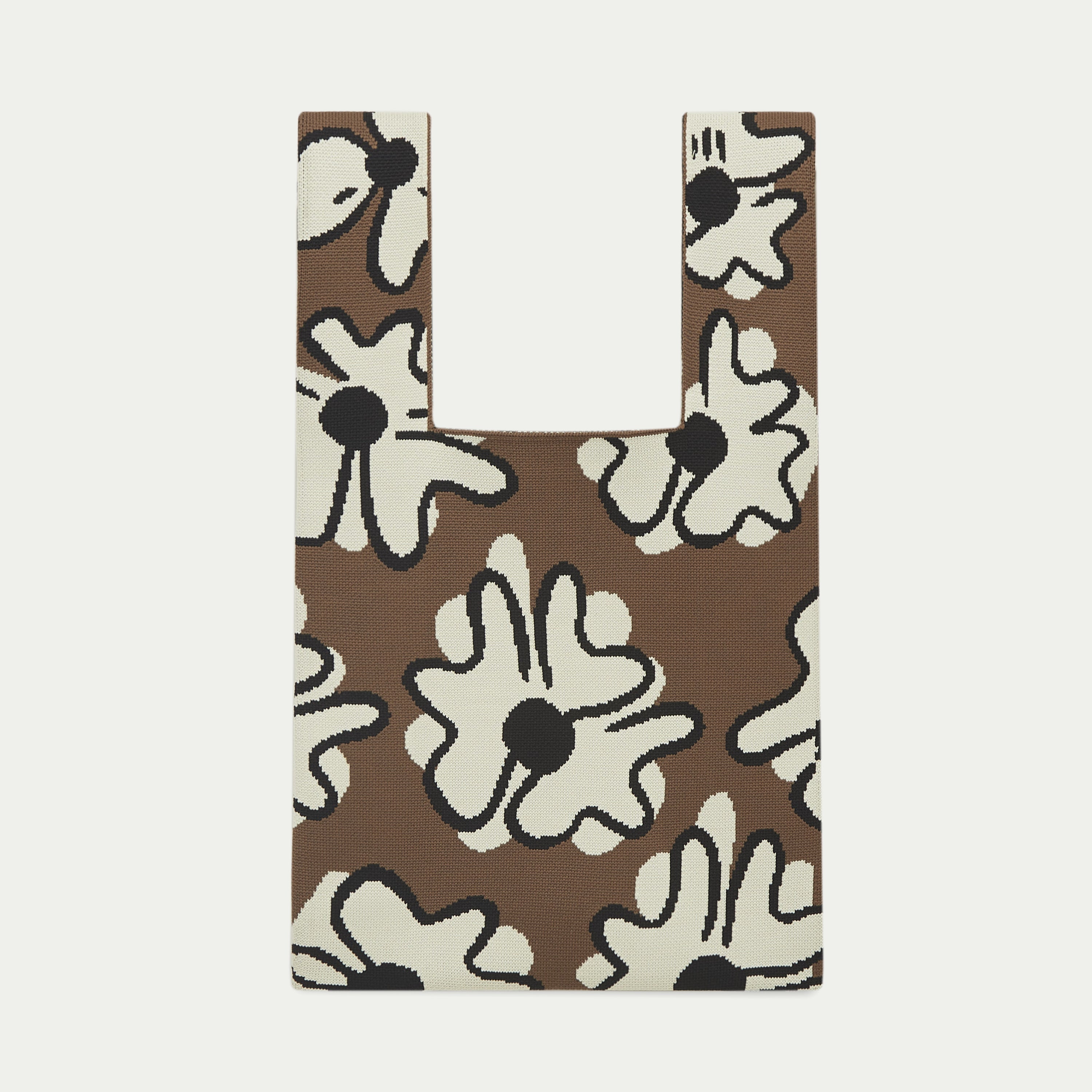 Brown knit tote bag featuring a bold graphic floral pattern with white flowers and black outlines, showcasing a statement all-over design.