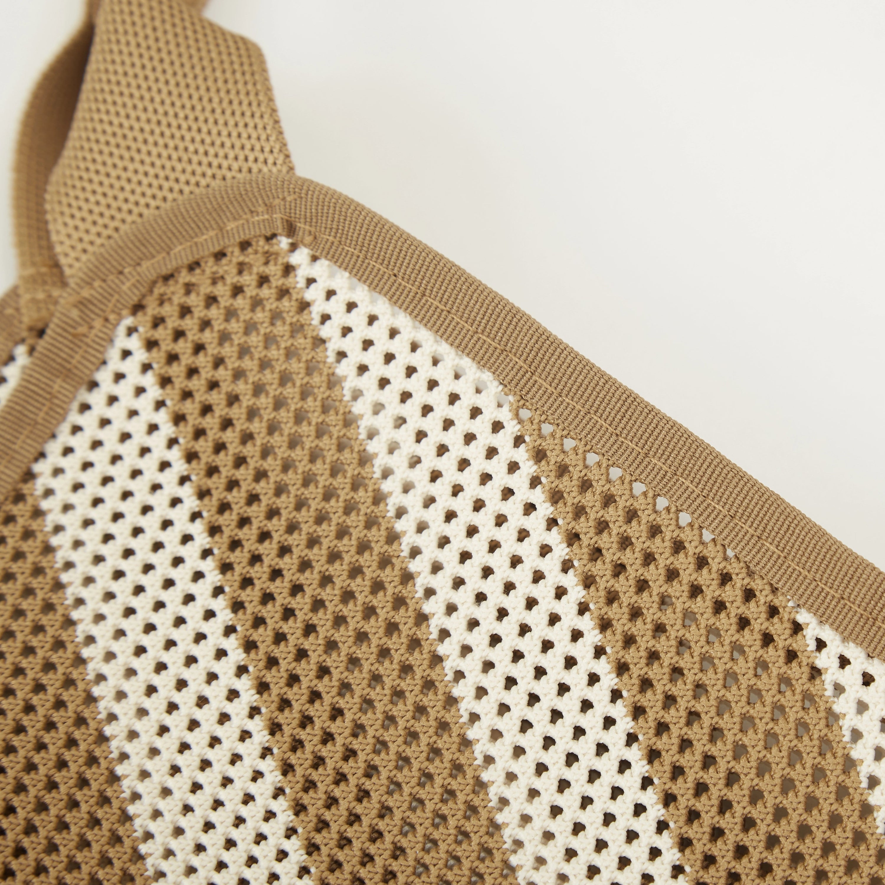 Close-up view of camel beige and white striped mesh knit tote bag showing open knit texture and top edge finishing.