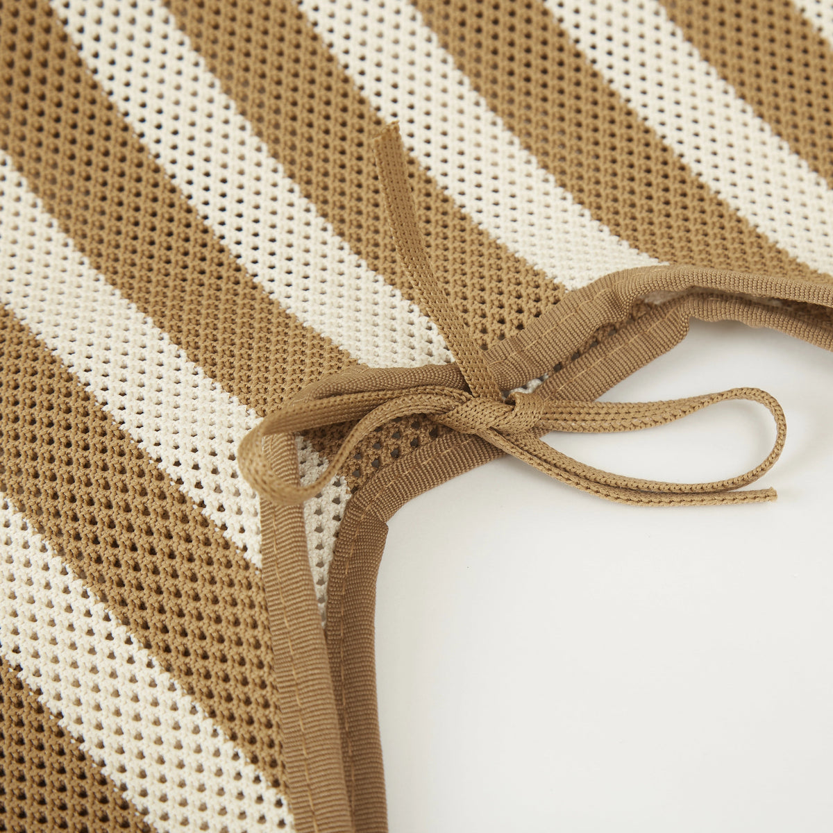 Close-up of camel beige striped mesh knit tote bag corner showing the knitted construction, edge binding, and tie detail.