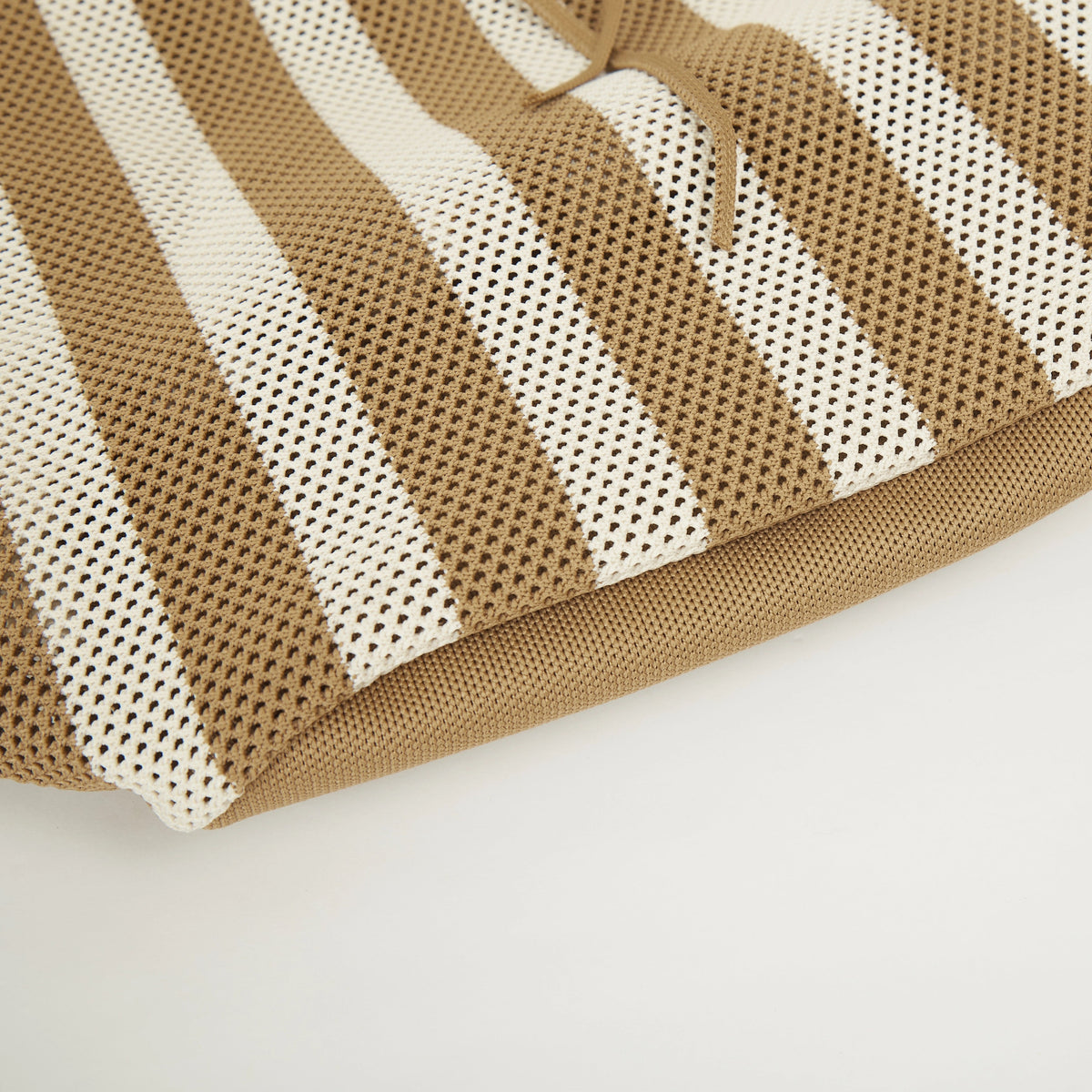 Bottom detail of camel beige and white striped mesh knit tote bag showing the soft knitted base and naturally formed folds from the flexible material.