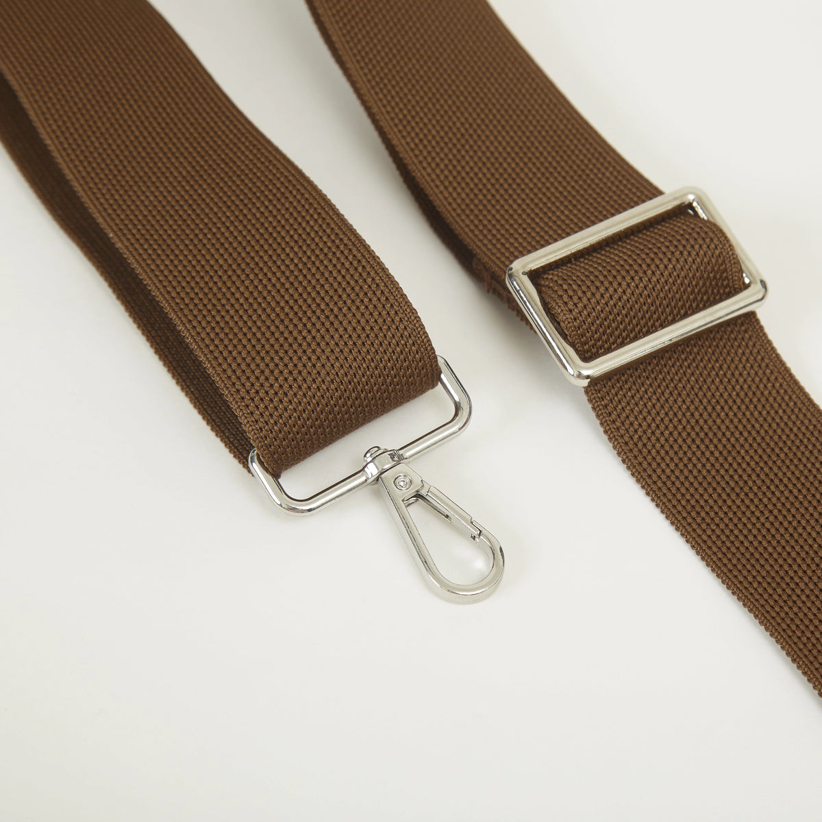 Close-up of the adjustable brown shoulder strap with metal buckle on a knit crossbody bag.