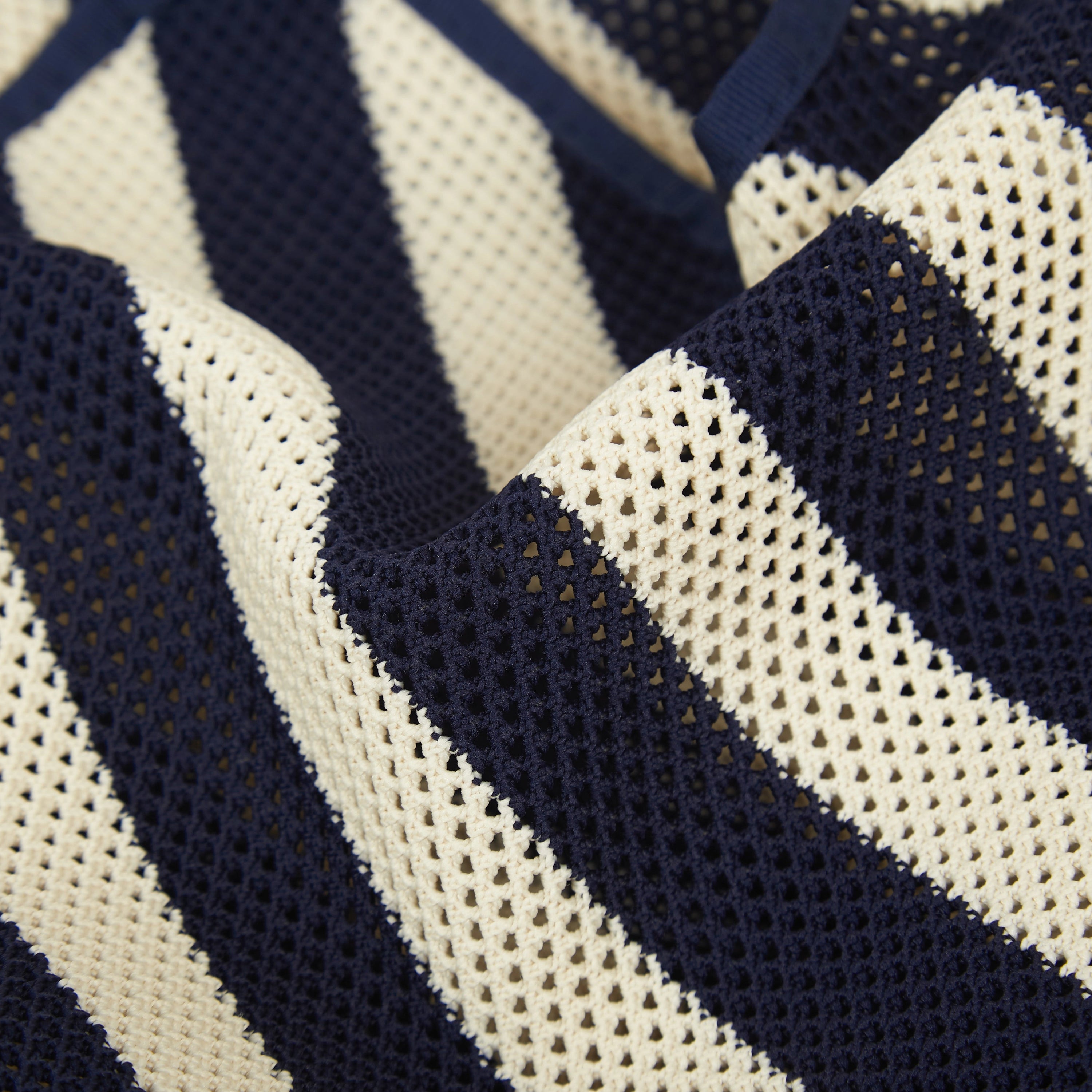 Close-up of navy and beige striped mesh knit tote bag corner showing the flexible knitted construction and finished edges.