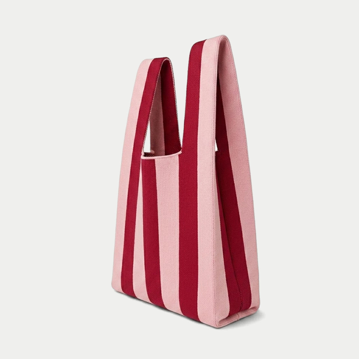 Side view of pink and red vertical stripe knitted tote bag showing the structured silhouette, handle design and textured knit construction.