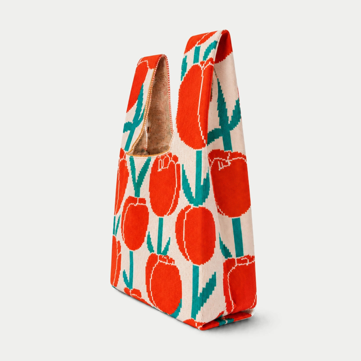 Side view of red, cream and teal tulip pattern knitted tote bag showing the bag profile, side depth and textured knit construction.