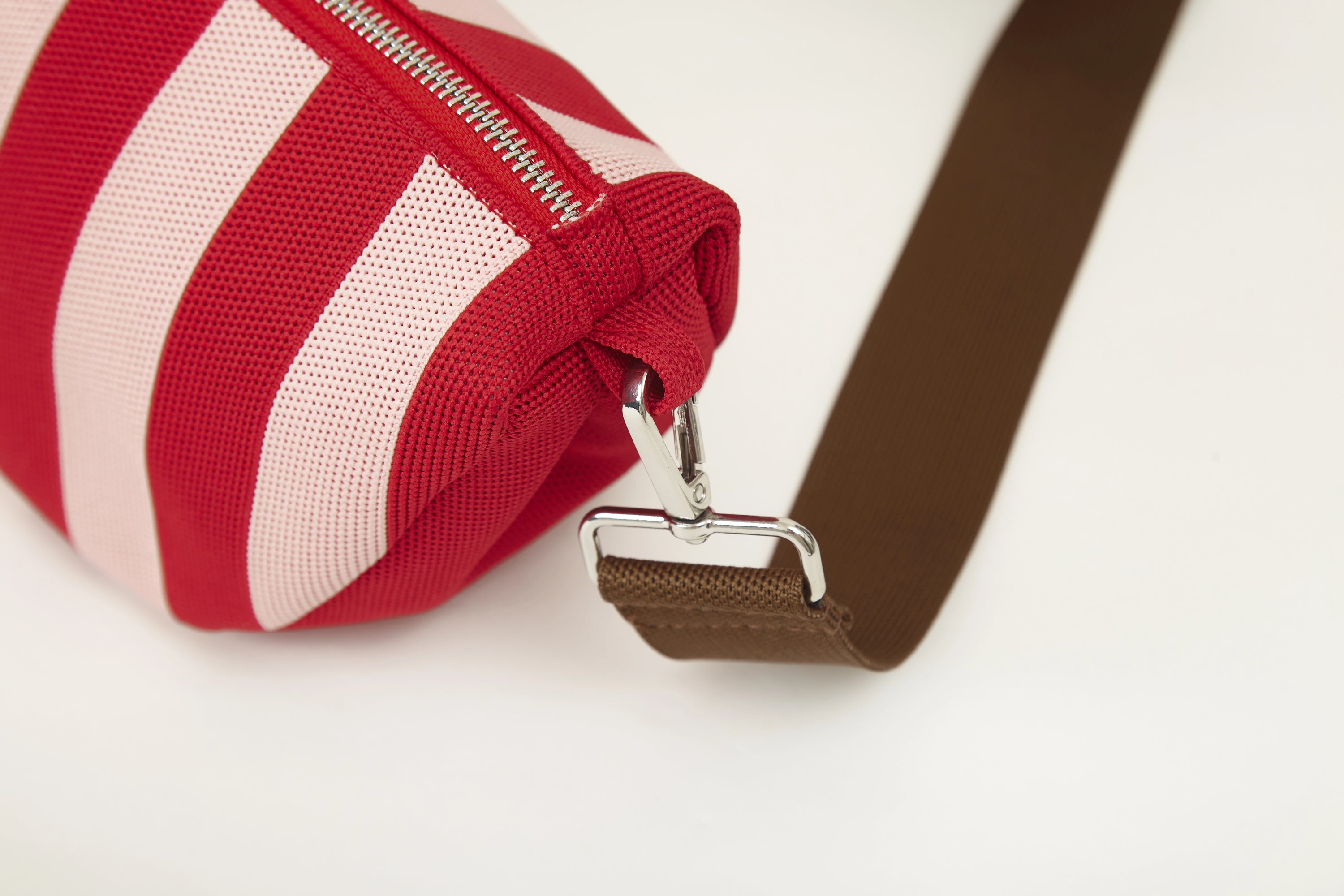 Red vertical stripe knitted half moon crossbody bag close-up showing silver metal hardware, strap attachment and woven fabric details.