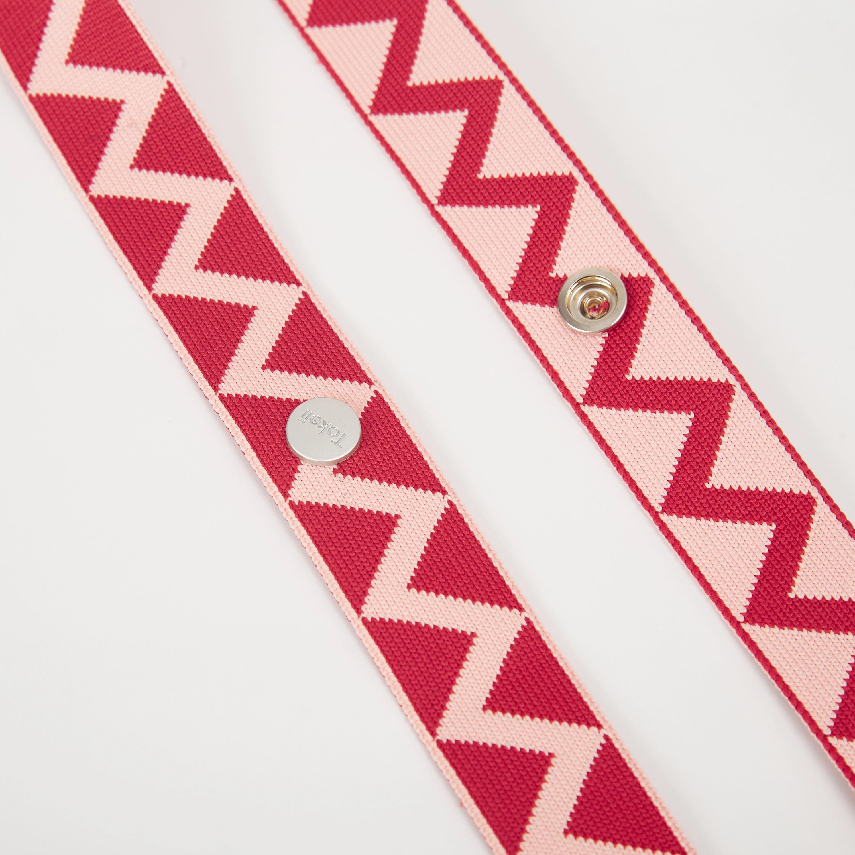 Detail view of red patterned bag strap featuring repeating zigzag motifs and metal hardware.
