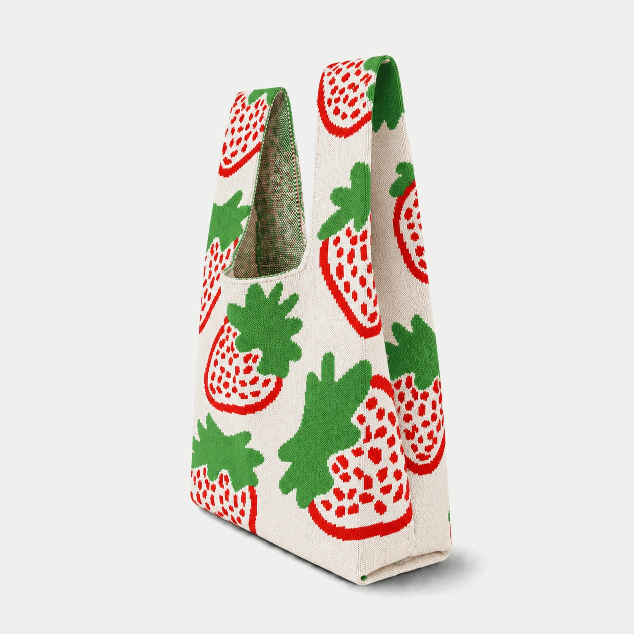 Side view of cream strawberry pattern knitted tote bag showing the wide handles, structured side depth and repeating red and green design.
