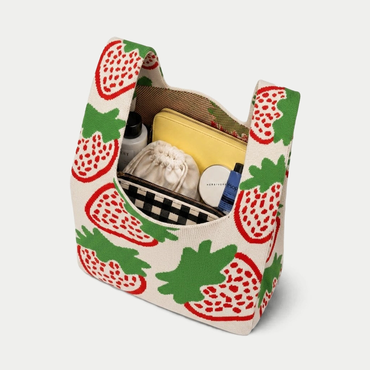 Top view of cream strawberry pattern knitted tote bag showing its capacity for carrying pouches, cosmetics and everyday essentials.