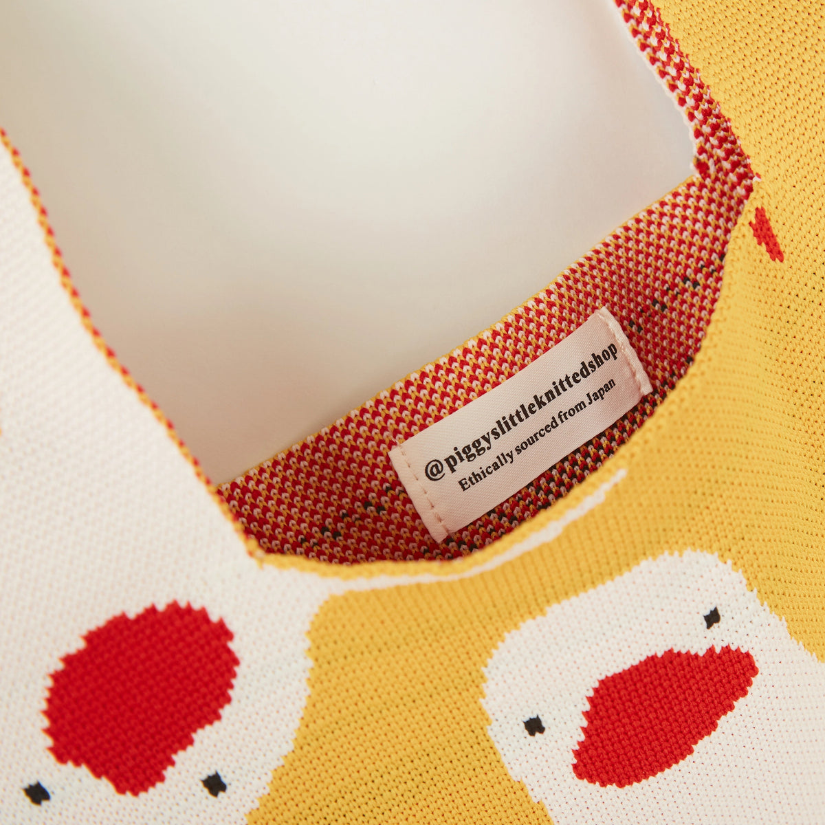 Close-up of the brand label inside the yellow duck knit tote bag with visible knitted fabric texture.